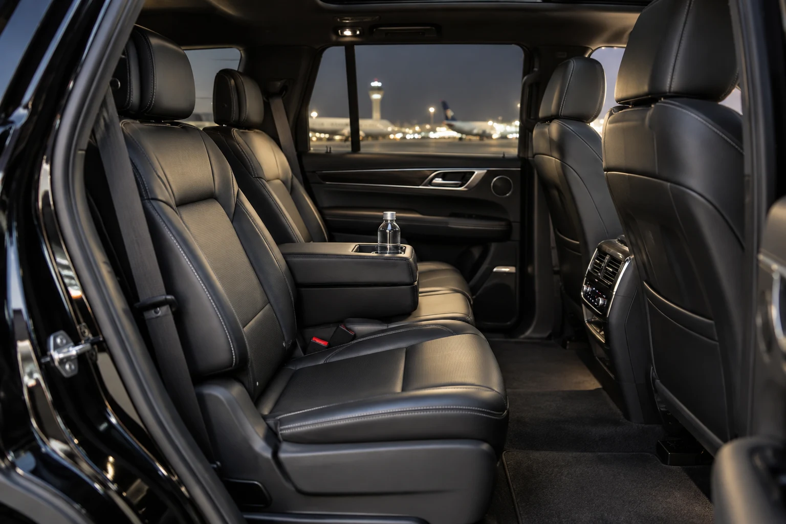 Premium SUV cabin with black leather passenger seats and airport lights outside.